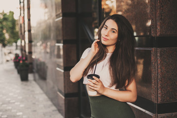 Beautiful smiling woman drink coffee walking on the city in summer day.