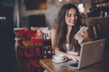Business woman using phone, working on a laptop and drinking coffee in a cafe.