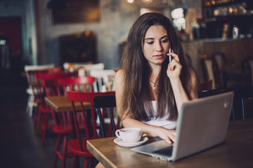 Business woman talking to the phone, working on a laptop and drinking coffee in a cafe.