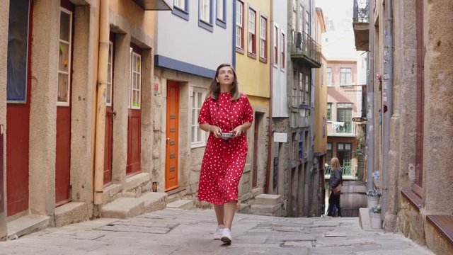 Young woman, tourist is taking photos of beautiful old european street on vintage camera, walking in beautiful portuguese city spot, enjoying landmarks around and her adventure in Europe