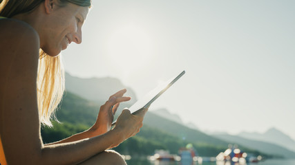 Young woman sitting on a beach at sunrise browsing on her digital tablet