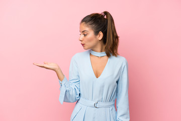 Young brunette girl over isolated pink background holding copyspace imaginary on the palm