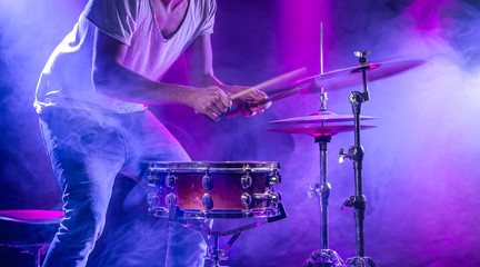 A drummer plays drums on a blue background. Beautiful special effects of light and smoke. The process of playing a musical instrument.