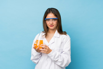 Young brunette girl over isolated blue background with a scientific test tube