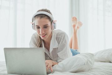 Woman relax on the bed using laptop and listening the music with headphones.