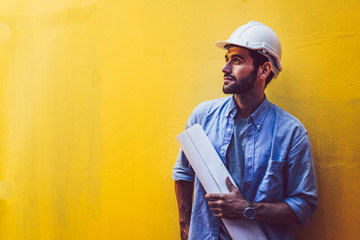 Young engineer carry blueprint at yellow background