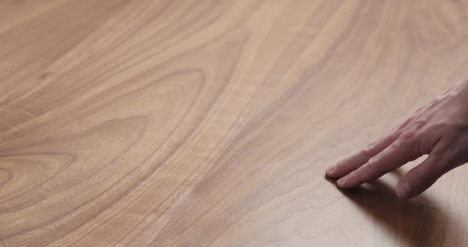 Slow motion man hand touches black walnut dining table surface