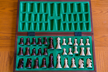 A wooden chess set in its box, view from above with brown background. The picture shows old traditional hand-made chess in a box