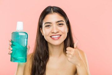 Young indian woman holding a mouthwash bottle smiling and raising thumb up