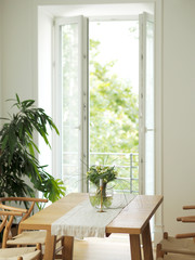 Fresh flowers in glass vase standing on a wooden table in white dining room interior with oriental carpet. Interior design in minimal style.