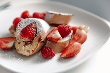 French toast with strawberries and raspberries, sprinkled with powdered sugar. Dessert on a white plate.