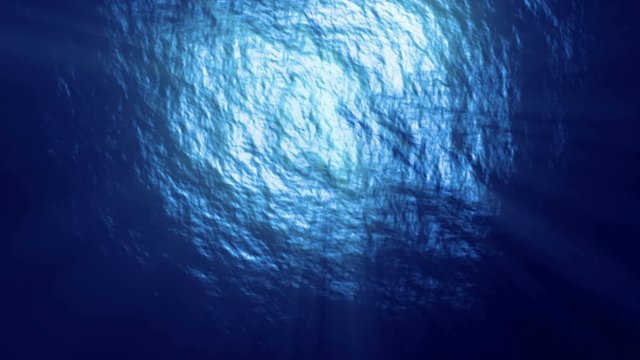 Under the deep blue sea, looking up at gentle waves on the surface with sun rays breaking through. Loopable footage.