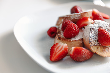 French toast with strawberries and raspberries, sprinkled with powdered sugar. Dessert on a white plate.