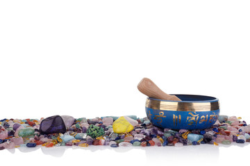 tibetan singing bowl and multicoloured healing chakra stones against a white background