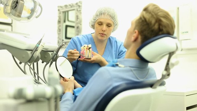Dentist in uniform with maket of jaw is telling about healthcare in dental clinic