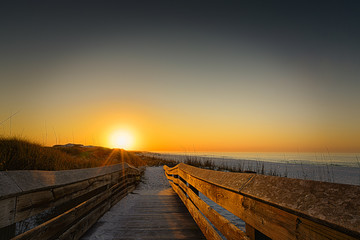 Warm sunrise casting a soft glow on the wooden walkway at the beach