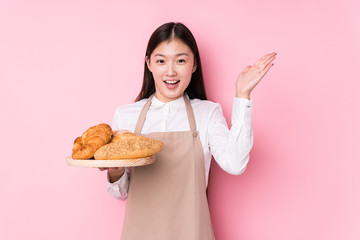 Young chinese baker woman isolated receiving a pleasant surprise, excited and raising hands.