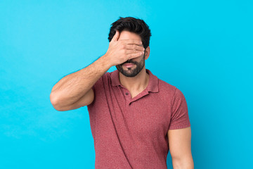 Young handsome man with beard over isolated blue background covering eyes by hands. Do not want to...