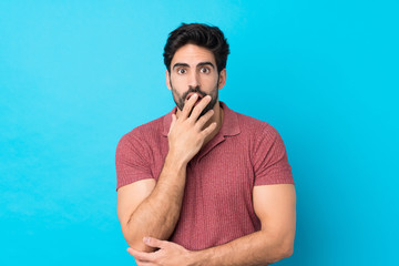 Young handsome man with beard over isolated blue background surprised and shocked while looking right