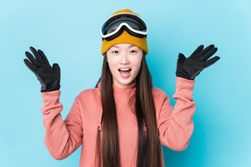 Young chinese woman wearing ski clothes isolated receiving a pleasant surprise, excited and raising hands.