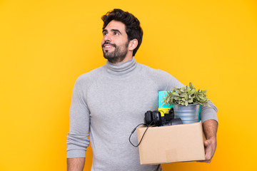 Young handsome man with beard making a move while picking up a box full of things over isolated...