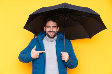Man holding an umbrella over isolated yellow background and pointing it