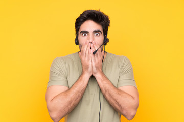 Telemarketer man working with a headset over isolated yellow background with surprise facial...