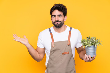 Gardener man with beard over isolated yellow background having doubts with confuse face expression