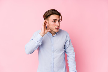 Young caucasian man posing in a pink background isolated trying to listening a gossip.