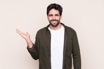 Young handsome man with beard over isolated background holding copyspace imaginary on the palm to...
