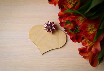 Red flowers, wooden heart and pink bow with sequins on white wooden background, selective focus, copy space. Valentines day, 8 March, Mother day background. Composition with flowers, top view. 