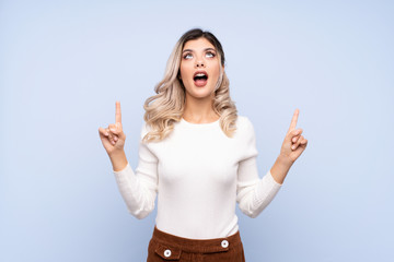 Young teenager girl over isolated blue background surprised and pointing up