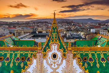 Budapest, Hungary - Aerial view of the famous colorful rooftop of State Treasury building with Fisherman's Bastion and golden sunset at background. Roof tiles has been made from Zsolnay pyrogranite - obrazy, fototapety, plakaty