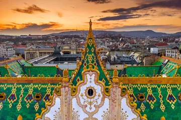 Fotobehang Budapest, Hungary - Aerial view of the famous colorful rooftop of State Treasury building with Fisherman's Bastion and golden sunset at background. Roof tiles has been made from Zsolnay pyrogranite © zgphotography