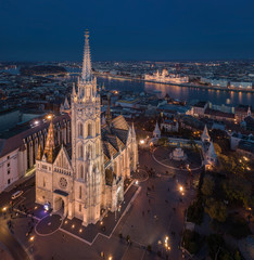 Naklejka premium Budapest, Hungary - Aerial drone view of the beautiful illuminated Matthias Church at blue hour with Fisherman's Bastion (Halaszbastya) and Parliament of Hungary at background
