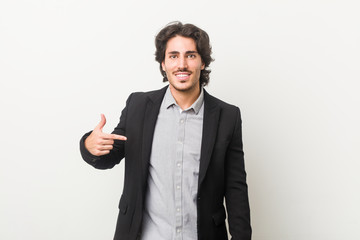 Young business man against a white background person pointing by hand to a shirt copy space, proud and confident