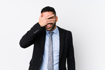 Young latin business woman against a white background isolated blink at the camera through fingers, embarrassed covering face.