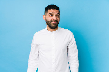 Young latin man against a blue  background isolated dreaming of achieving goals and purposes