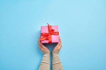two female hands in a sweater hold closed square pink box with a bow
