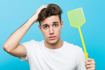 Young caucasian man holding a fly swatter being shocked, she has remembered important meeting.