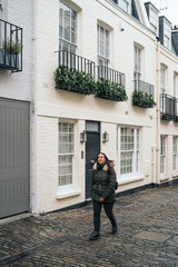 Young woman walking and use smartphone in a Exclusive mews with white small houses in Chelsea, a wealthy borough of London.