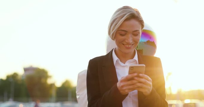 Close up of the young Caucasian pretty woman texting or tapping on the smartphone while funny astronaut going around her and looking at the screen what she doing. Outdoors.