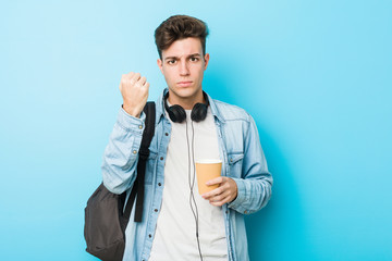 Young caucasian student man holding a take away coffee showing fist to camera, aggressive facial expression.