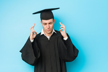 Young caucasian graduated man crossing fingers for having luck