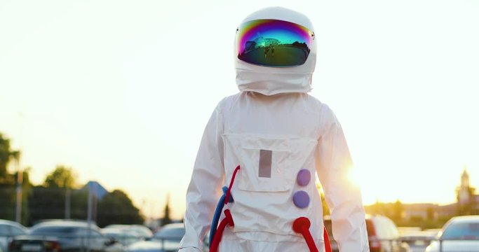 Portrait shot of the person in the astronaut costume and with a head armor standing in front of the camera. Outside at the parking.