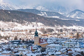 Winter cityscape of alpine city Schladming with orange church in the middle. Skiing heart of the Schladming Dachstein region, Styria, Austria, Europe. Snow-capped mountains at the background.