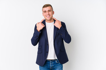 Young business caucasian man smiles, pointing fingers at mouth.