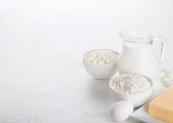 Fresh dairy products on white table background. Glass jar of milk, bowl of cottage cheese and baking flour. Eggs and cheese. Space for text