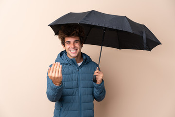Man holding an umbrella over isolated background inviting to come with hand. Happy that you came