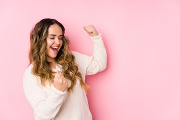 Young curvy woman posing in a pink background isolated raising fist after a victory, winner concept.